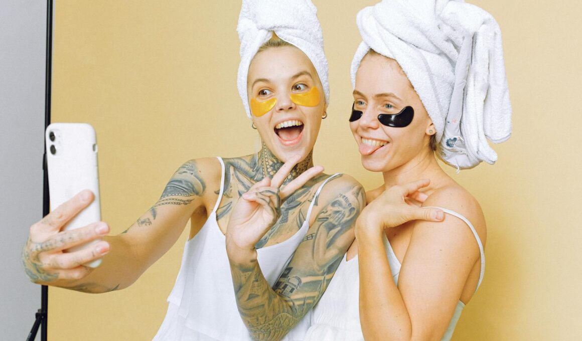 Two women enjoying a skincare routine with facial masks, taking a selfie wrapped in towels against a beige background.